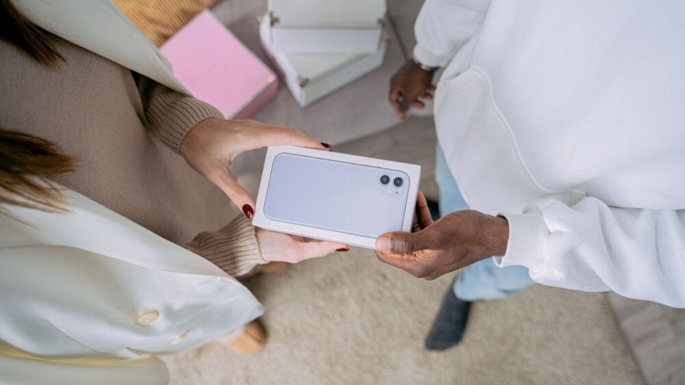 Två personer håller en förpackad smartphone med dubbla kameror