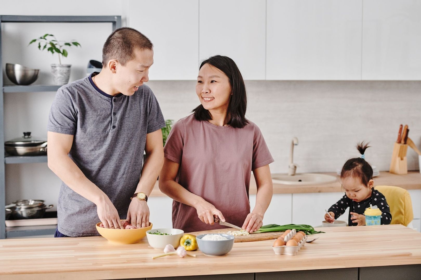 Två vuxna lagar mat medan ett barn sitter bredvid i köket